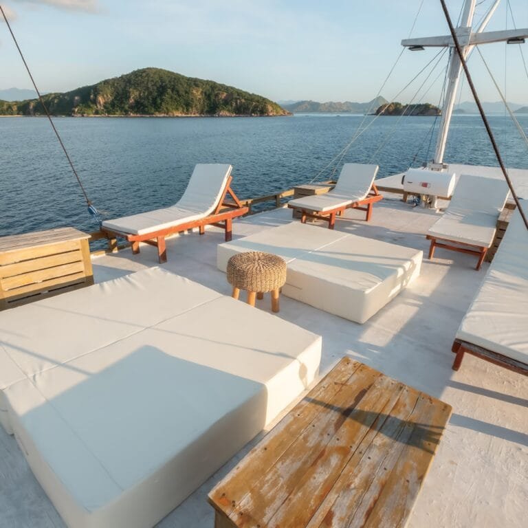 a deck of a boat with chairs and a table on the water