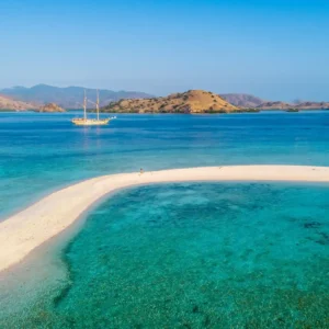 a white sand beach with a sailboat in the water